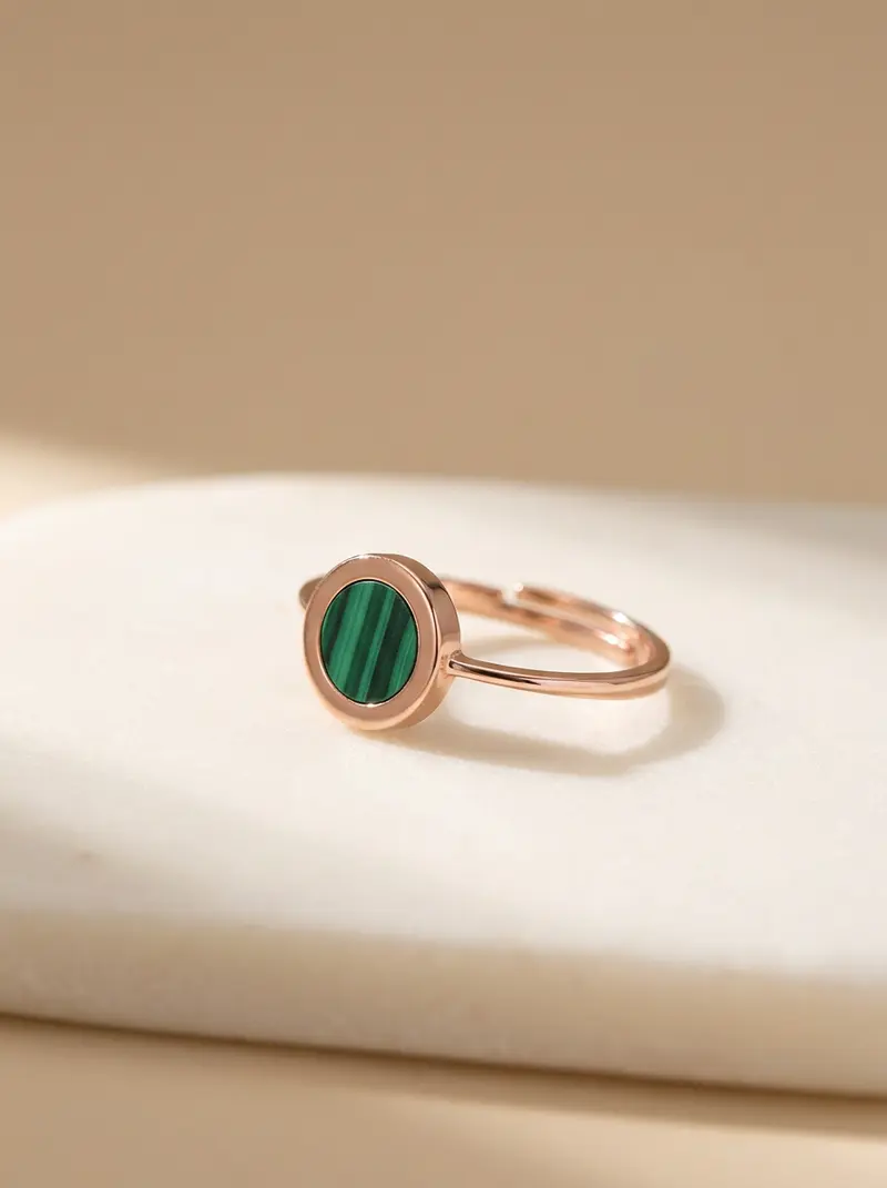 Malachite round ring with a rose-gold finish resting on an ivory slab