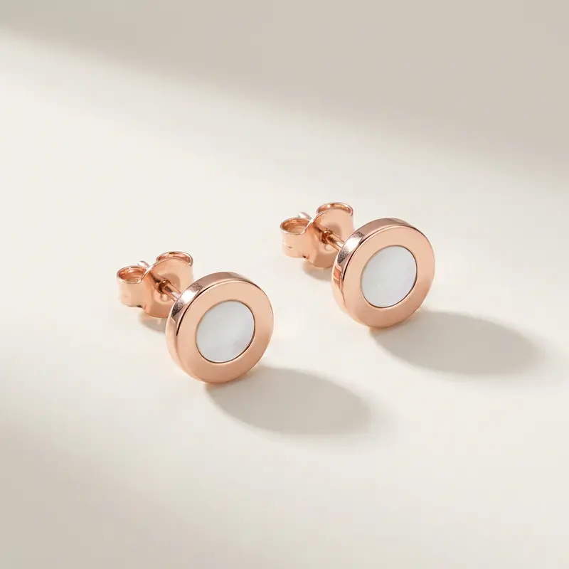 Pair of round mother-of-pearl studs on a warm off-white surface