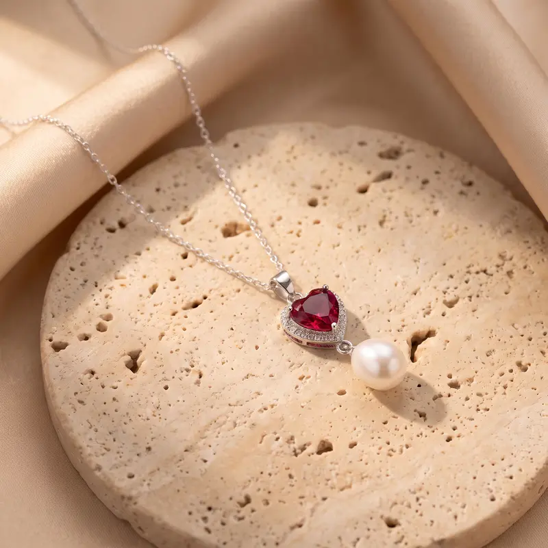 Ruby-red heart and pearl pendant resting on a travertine disc